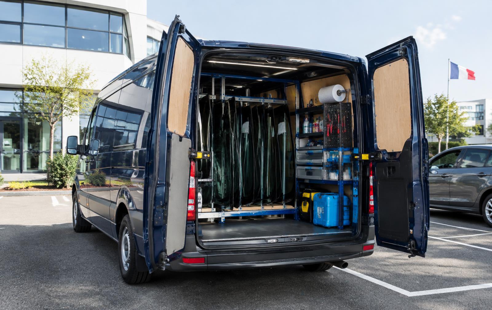 Camion atelier aux portes ouvertes, équipé de racks de pare-brise, sur un parking d'entreprise